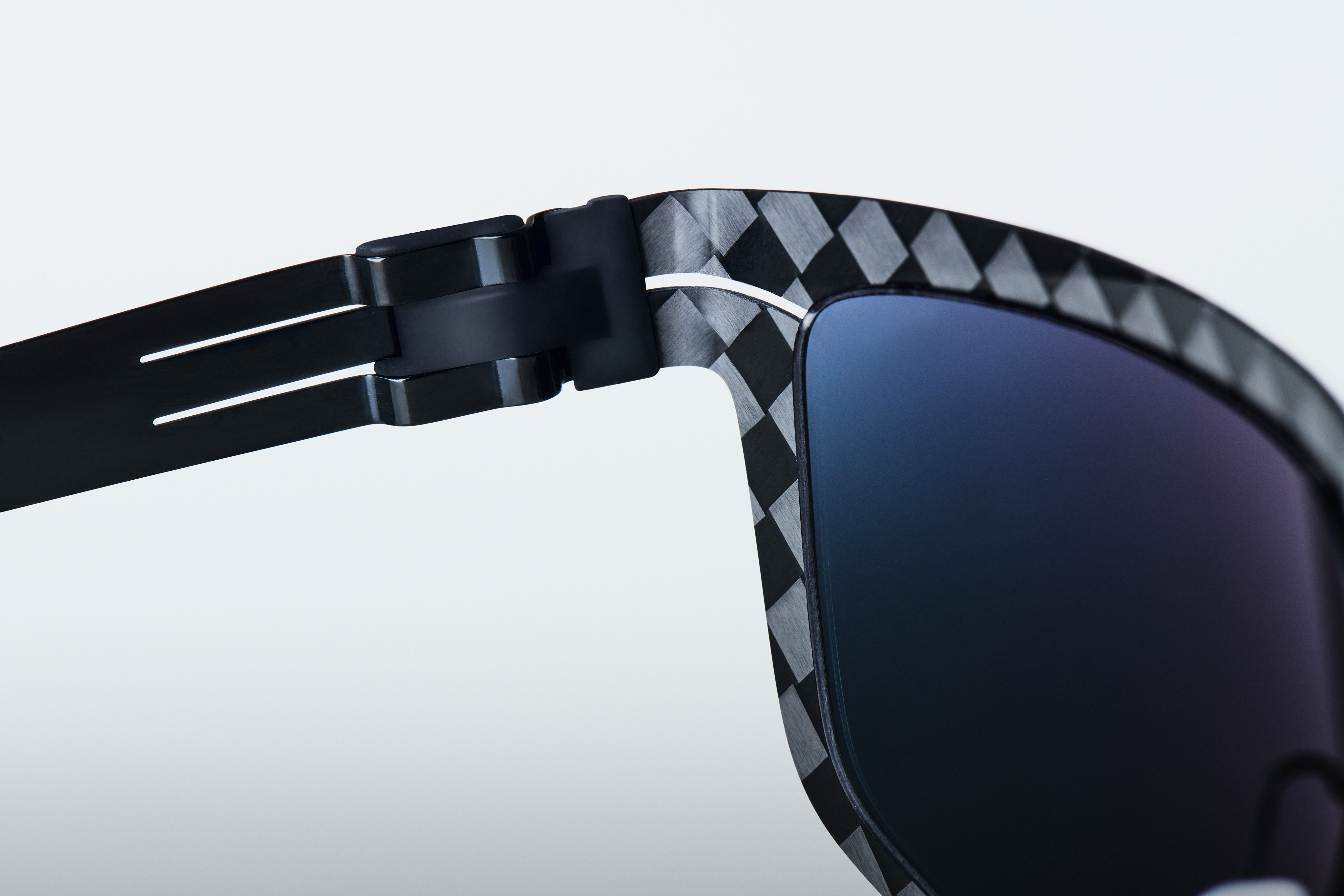 Close-up of ic! berlin FLEXARBON carbon fiber frame showing the distinctive woven pattern exterior and FLEX clip hinge mechanism — aerospace-inspired ultra-lightweight eyewear